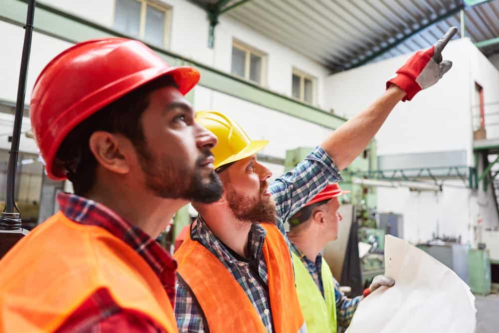 Three construction workers in hard hats pointing at a plan for the Expansion Approval of Coastal Holiday Park in St. Audries Bay.
