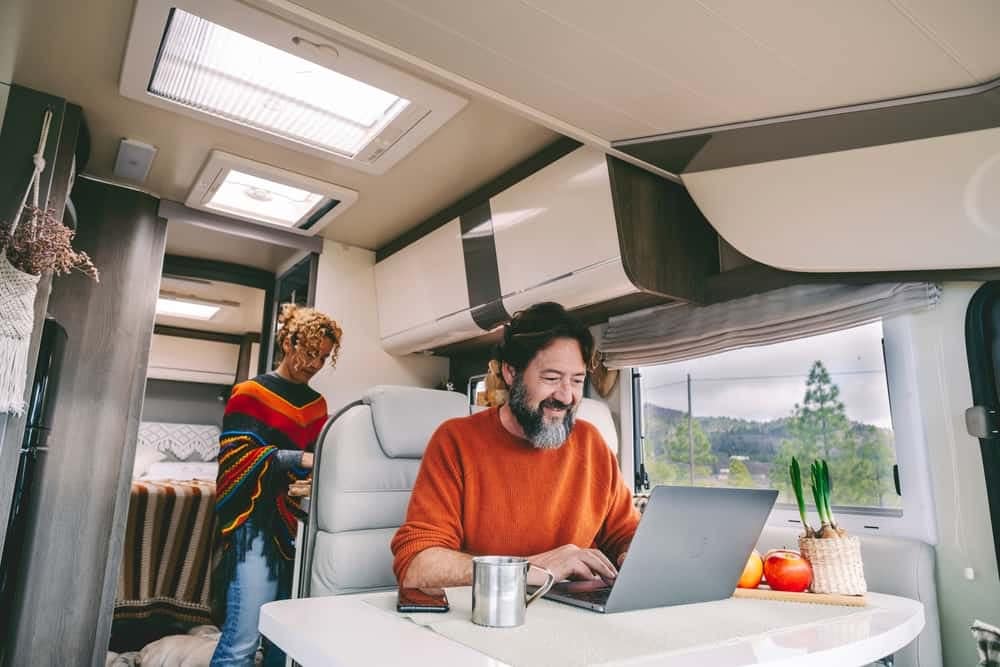 A man and woman, Homeworkers, working on a laptop in a Jayco RV.
