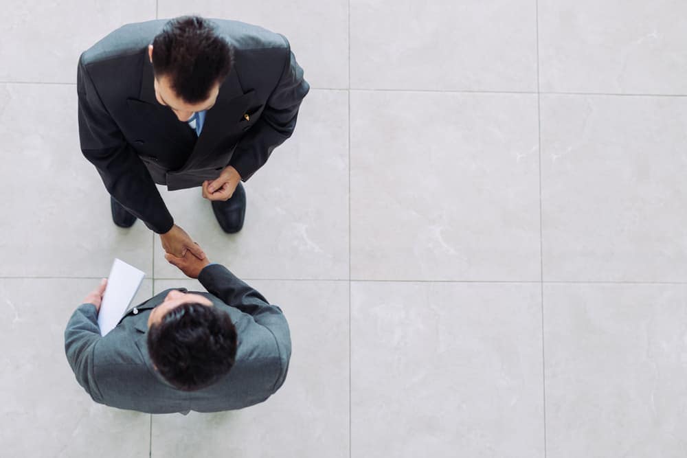 Two businessmen shaking hands on a tile floor after finalizing a supply contract.