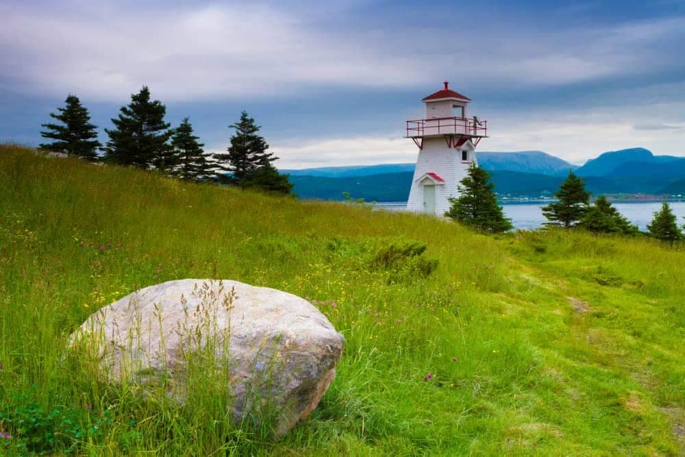 A lighthouse, maintained by the Canadian Gov't, sits on top of a grassy hill in Newfoundland and Labrador, attracting tourists from around the world.