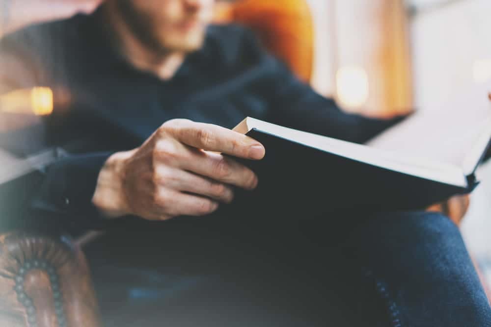 A man is sitting in a chair reading a book at a public library.