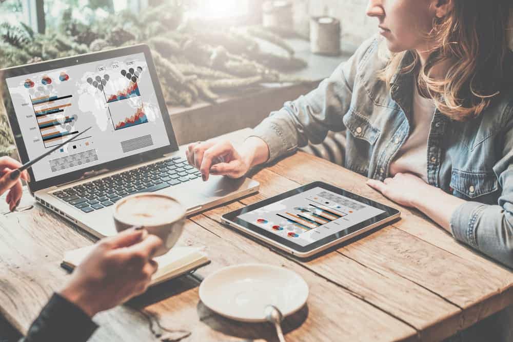 Two women sitting at a table analyzing campaign data on a laptop with graphs.