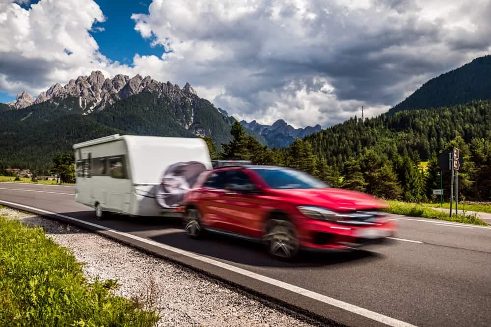 A red car towing a Sunland Caravans rv on a mountain road.