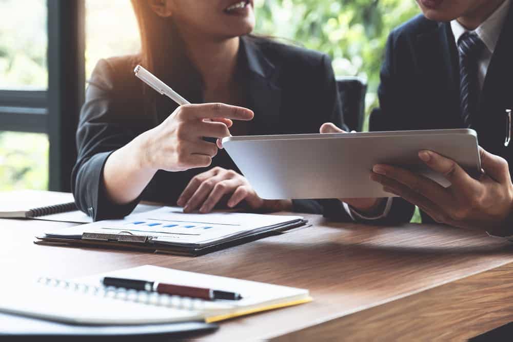 Two business people sitting at a table looking at a tablet.