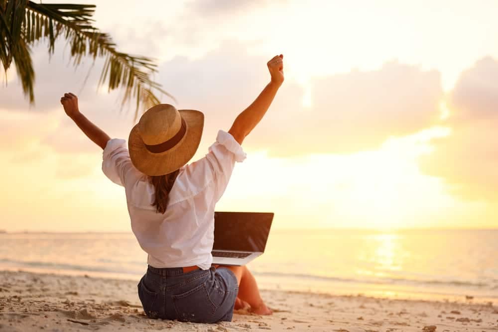 Woman with laptop on the beach at sunset, enjoying the peaceful ambiance while utilizing Airbnb Integration.