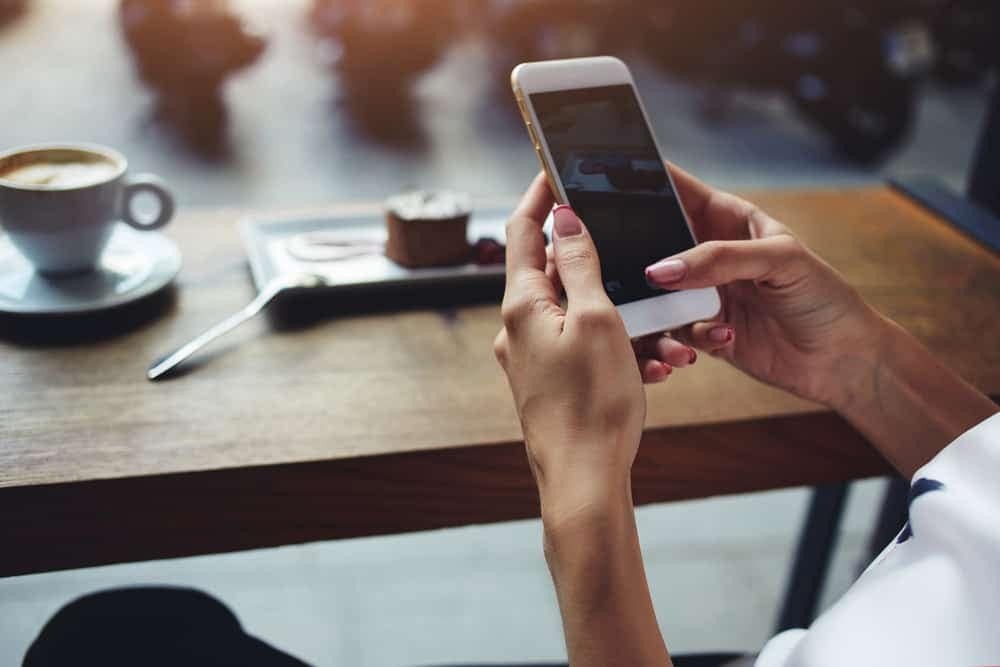 A woman using a mobile app while sitting at a table with a cup of coffee.