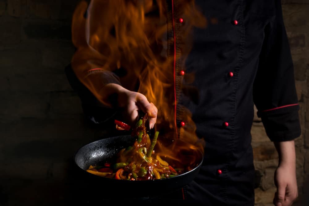 An Executive Chef in a black chef's uniform is cooking elevated food in a wok.