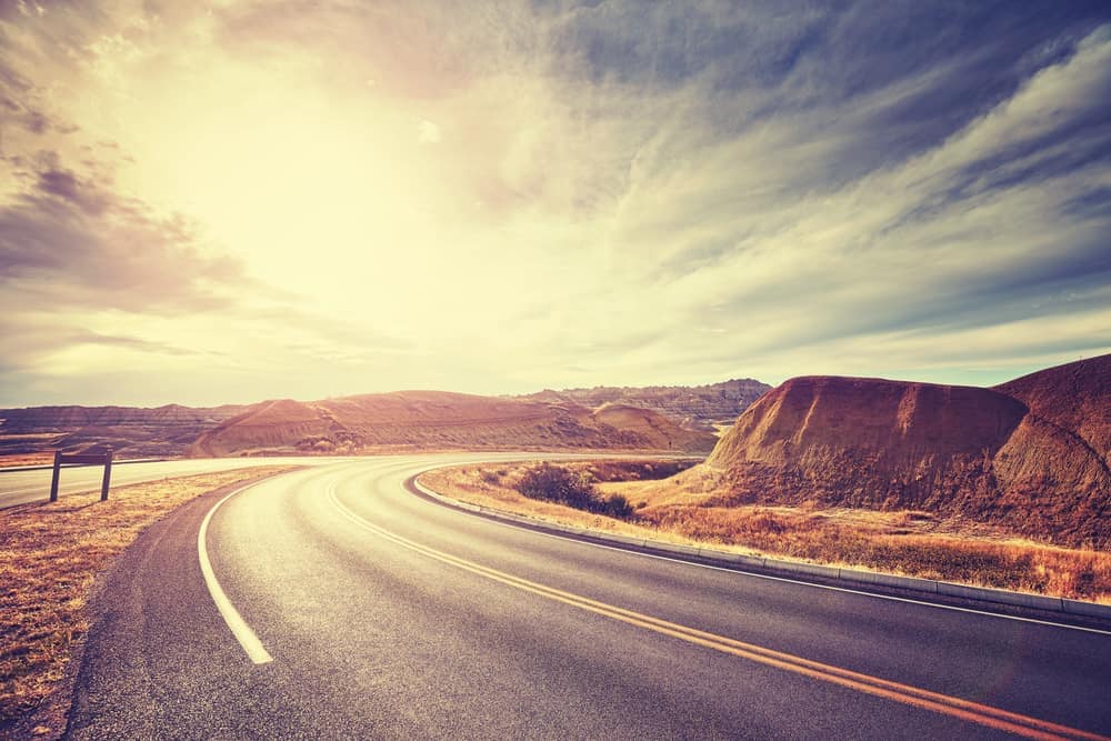 A scenic UK road trip through the desert, with the sun setting behind the expansive road. Experience the thrill of exploring new horizons while saving money on your journey with Camplify.