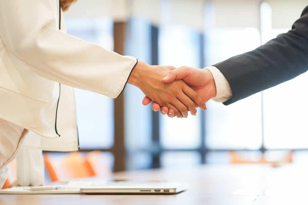 Two business people using a collaborative approach to shake hands in a conference room while discussing the Australian Caravan Industry and referencing the ACCC Report.