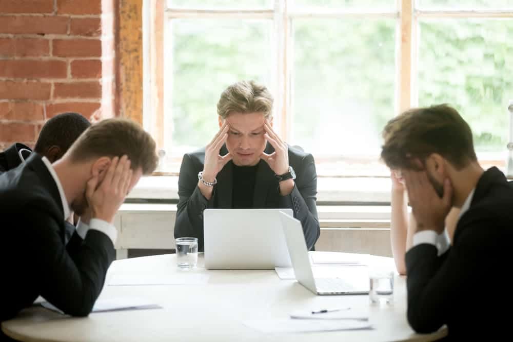A group of business people sitting around a table with their hands on their heads, discussing the impact of the recession in Canada.