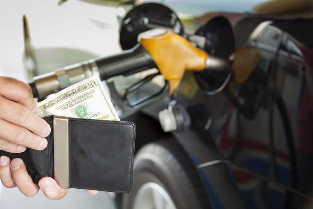 A man is filling up his car with gas. The costs drop below $4.