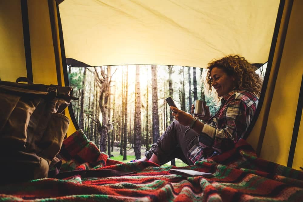 An irresponsible woman sitting in a tent looking at her phone while freedom camping in New Zealand.