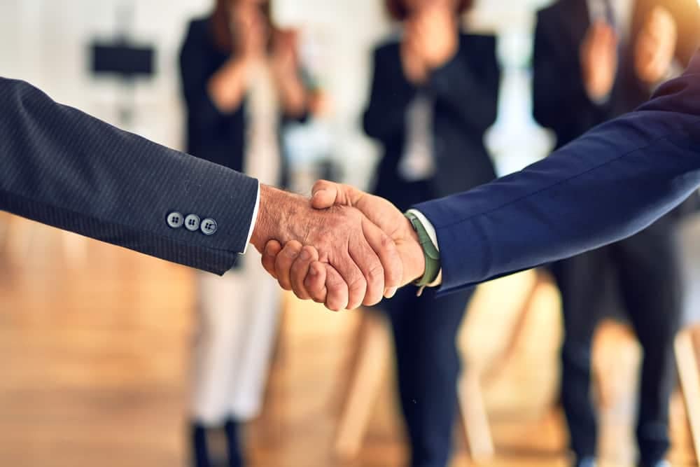Two business people shaking hands in front of a group of Camper City employees.
