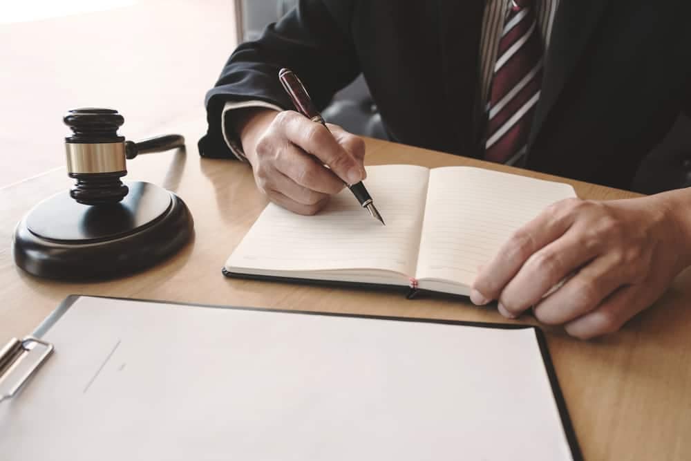 A man in a suit writing in a notebook with a gavel, focused on strengthening U.S. industries against foreign competitors in line with the CHIPS Act.