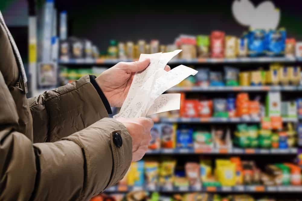 An American man is holding a receipt in a grocery store with lower prices.
