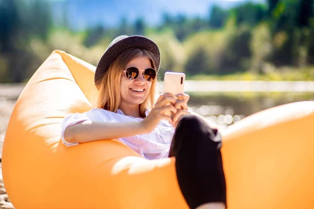 A woman sitting on an inflatable lounger, using her phone to access the new mobile app recently launched by Escapees RV Club.