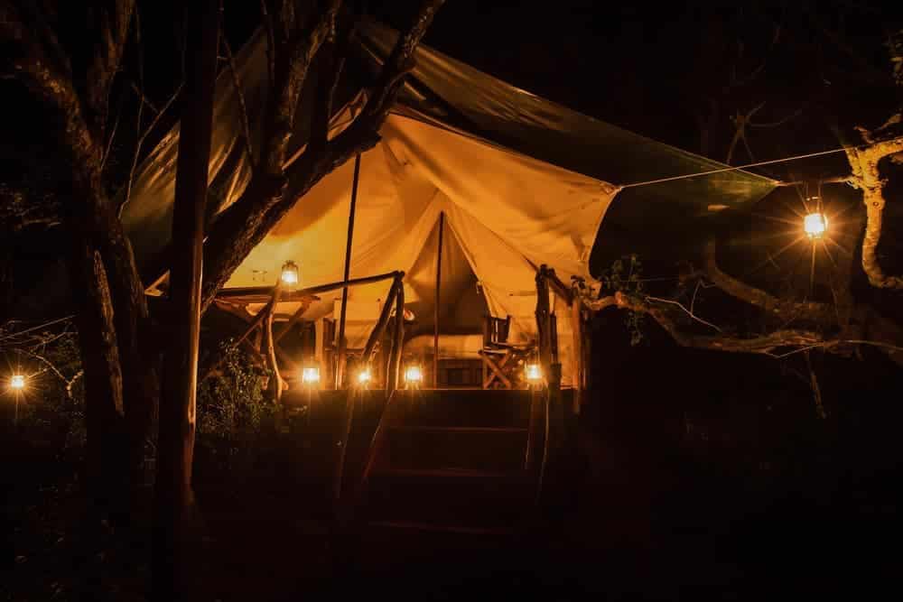A Safari-Style tent lit up at night in the woods.