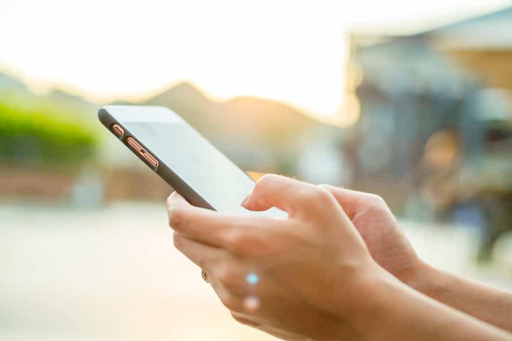 A woman's hand holding a cell phone in front of a building while using an online tool for near real-time wildfire info.