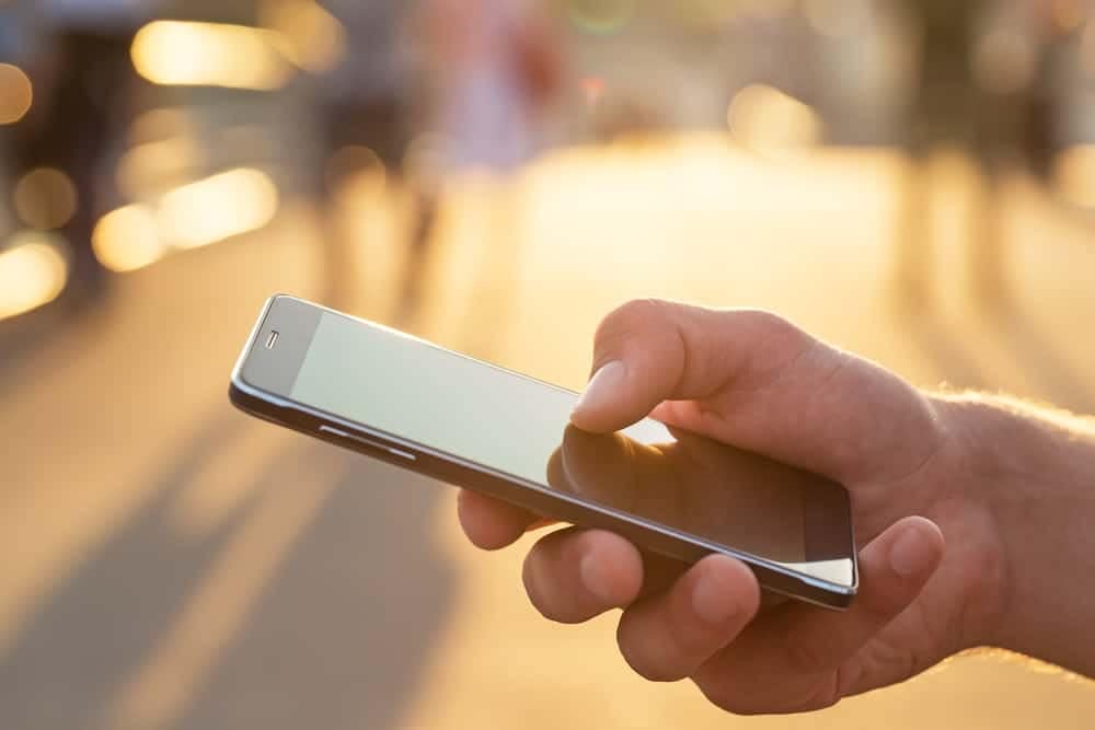 An  hand holding a smartphone in front of a group of people.