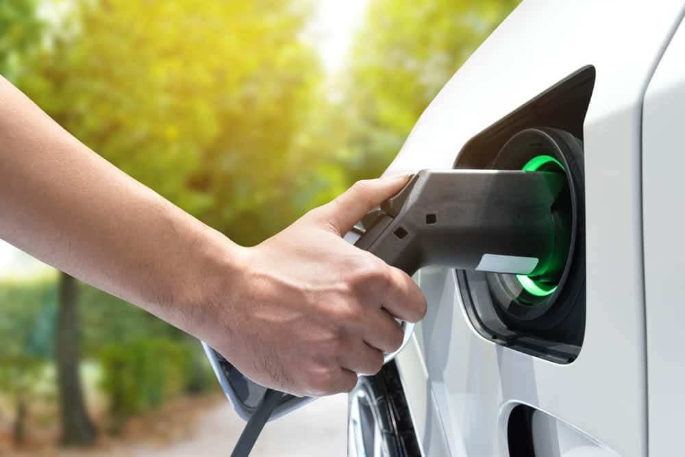 A person is taking advantage of outdoor recreation opportunities by charging an electric car in a parking lot.
