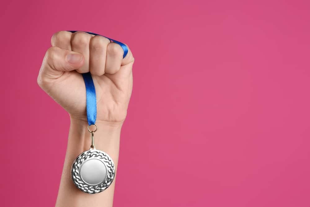 A woman's hand holding a Silver Medal of Honour on a pink background.