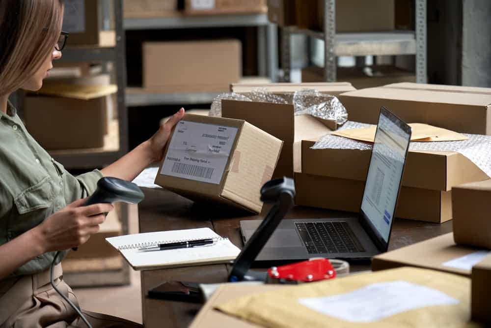 An Australian woman working at a European warehouse with boxes and a laptop, managing an Ecommerce Platform.