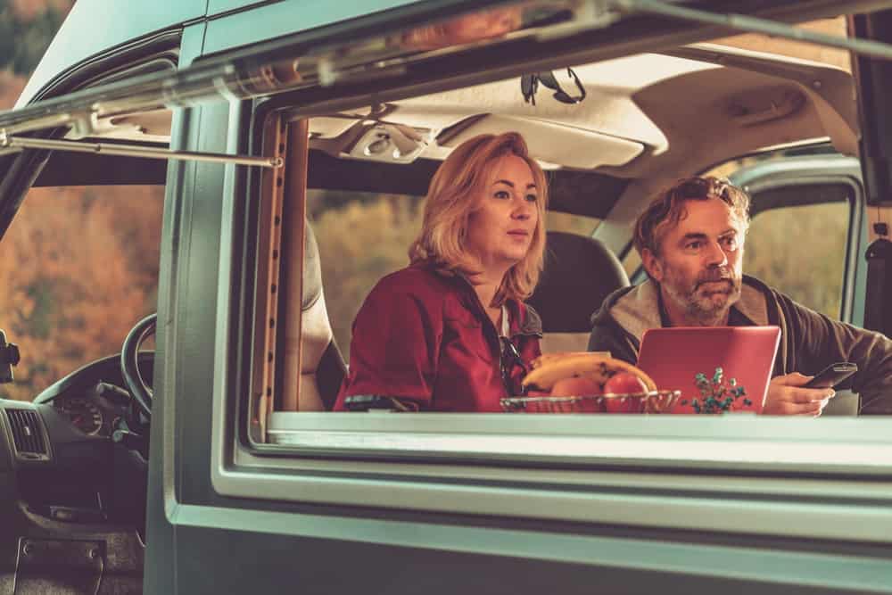 A man and woman sitting in a private outdoor cinema tv van with a laptop.