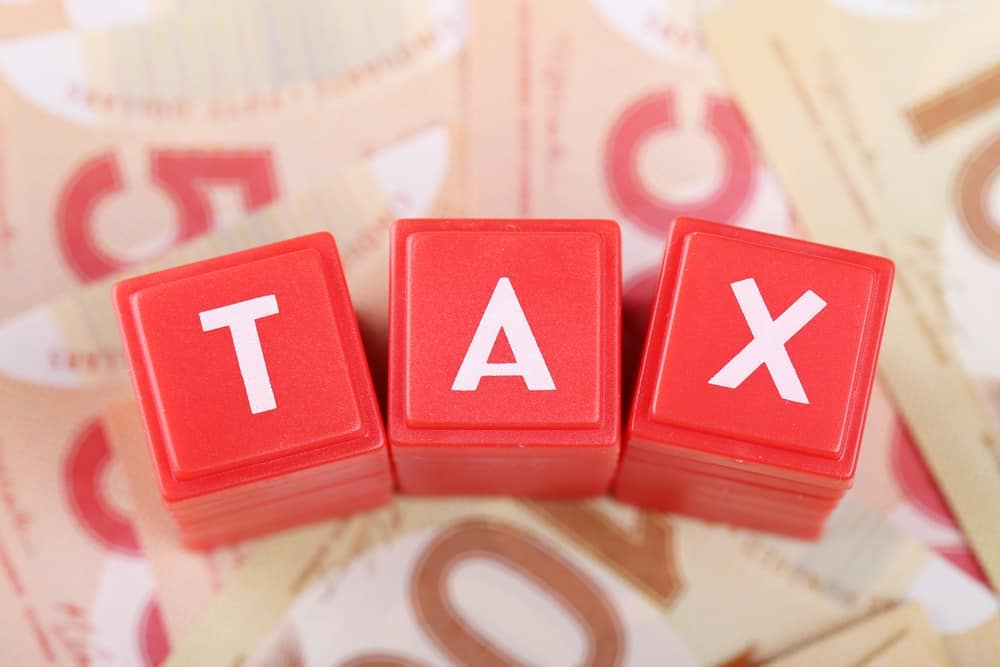 A red block with the word tax on top of a pile of money in Alberta.