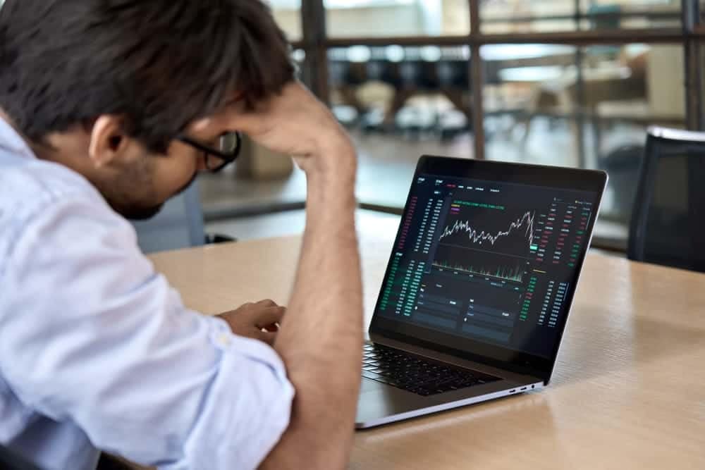 A man sitting at a desk looking at a laptop displaying a stock chart reflecting the lower US job gain in August.