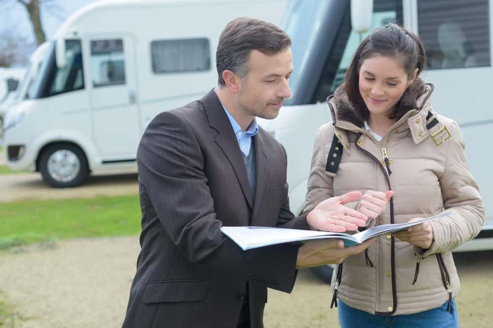 A man and woman, representing MBA Insurance, review a document together during the RV Dealers Convention/Expo at a scenic RV park.