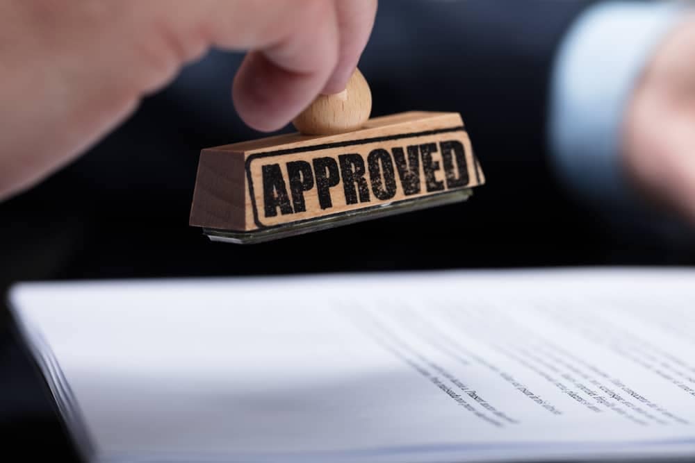 A man is holding a rubber stamp with the word compliance approval on it.