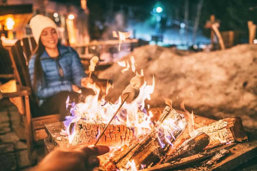 A couple enjoying a cozy campfire at night during their winter camping adventure.