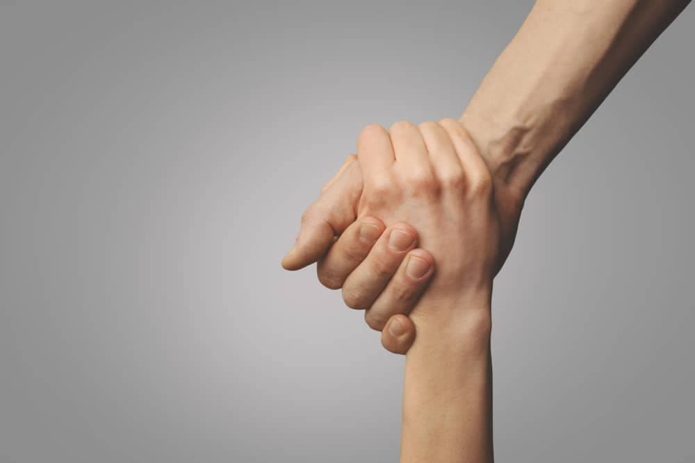Two hands holding each other on a gray background, providing support during difficult times with Service Canada's Employment Insurance.