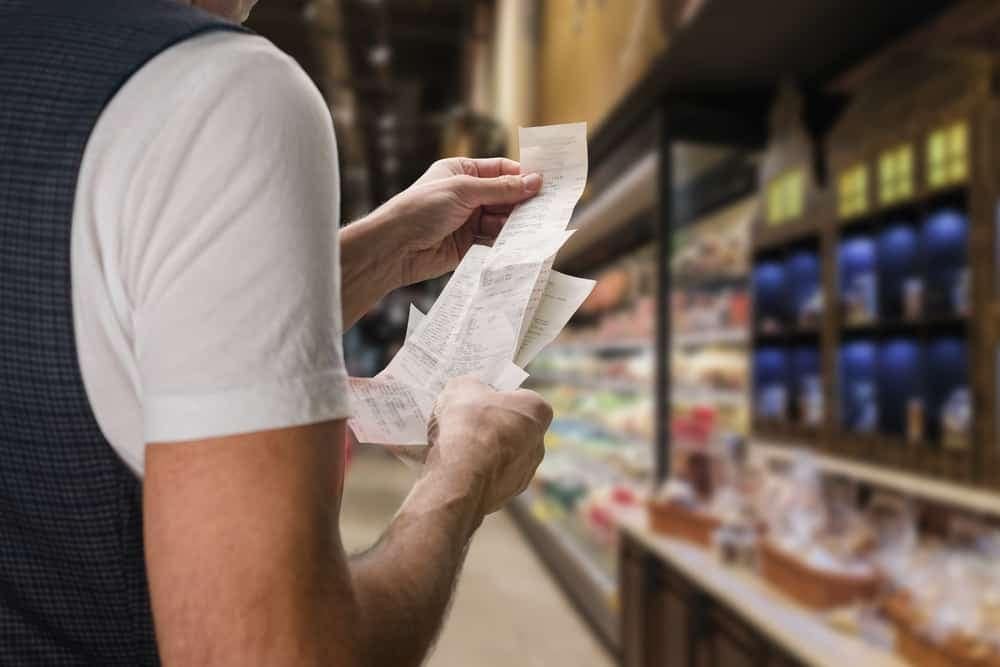 A man is looking at a receipt in a grocery store, showing the impact of inflation on consumer confidence.