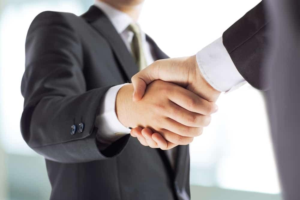 Two businessmen shaking hands in front of an office, symbolizing partnership.