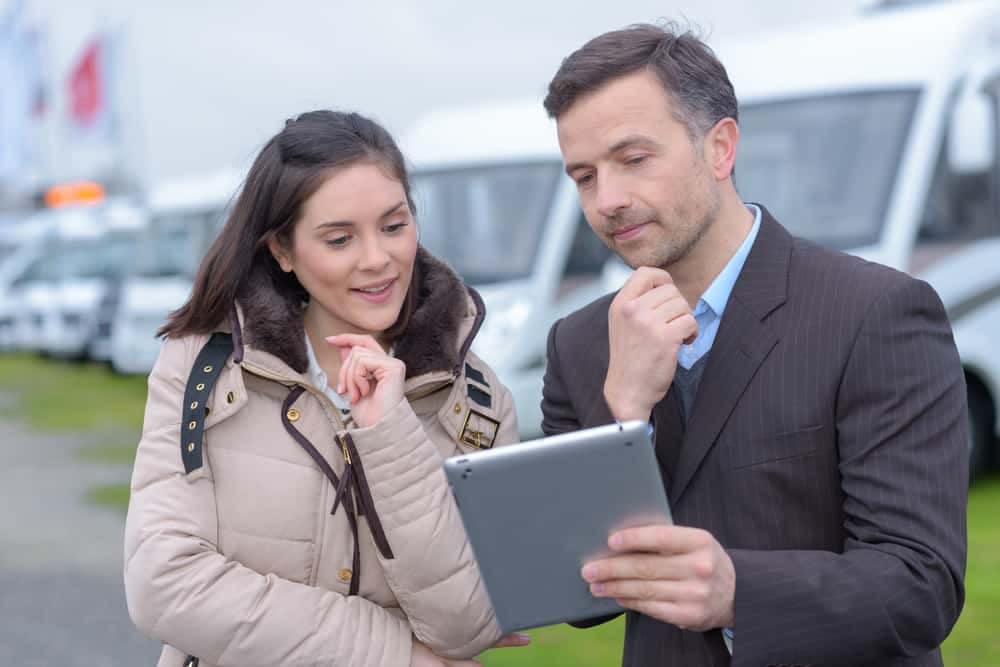 A man and woman, representing the RVIA, are analyzing the September RV shipments data on a tablet while standing in front of a group of RVs. They are comparing the figures Year-over-Year (