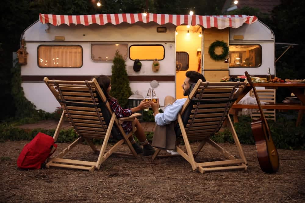 Two people sitting in chairs in front of a magic camper, enjoying an outdoor experience.