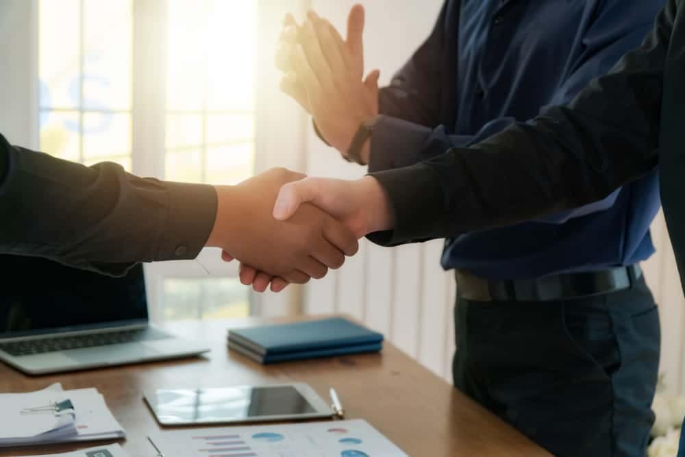 Two businessmen shaking hands at an office desk discussing the Palomino RV.