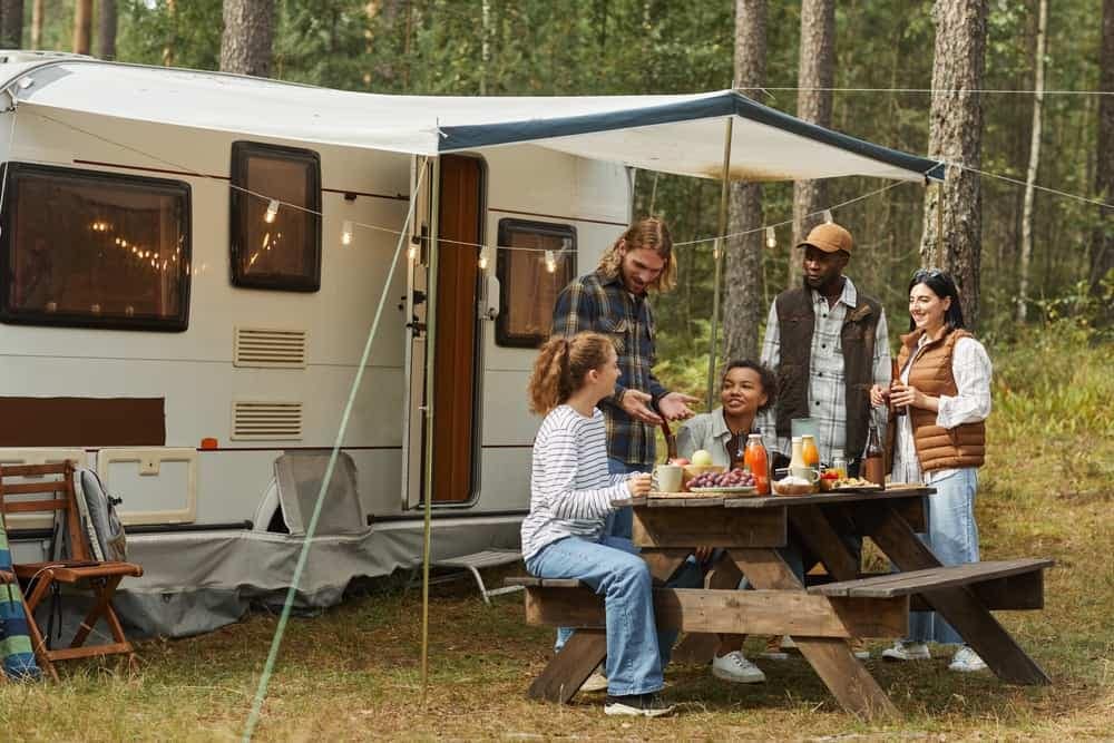 A group of outdoor enthusiasts sitting around a picnic table in the woods, enjoying their time together and embracing the beauty of nature.