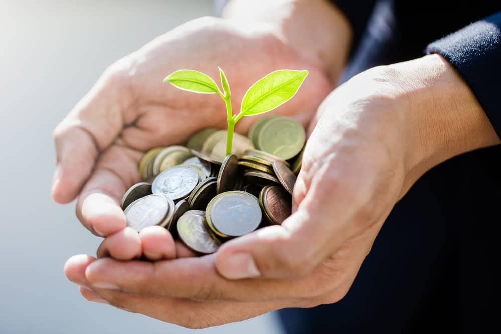 A man holding coins, symbolizing funding, with a plant growing out of them in the context of a Renewable Energy Project at Bargoed Farm.