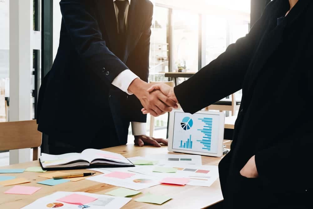 Patrick Industries acquires Transhield; two business people shaking hands in front of a table.
