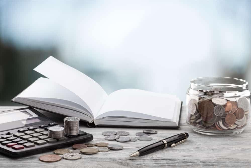 A jar of coins and a book on a wooden table.