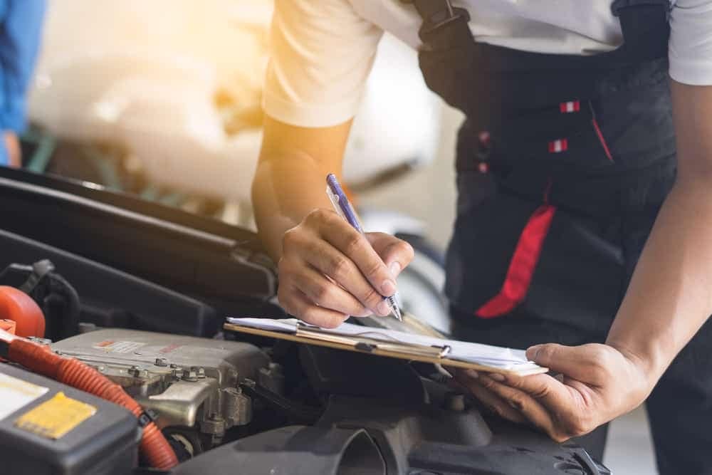 A mechanic working on a car with a clipboard and Winnebago.