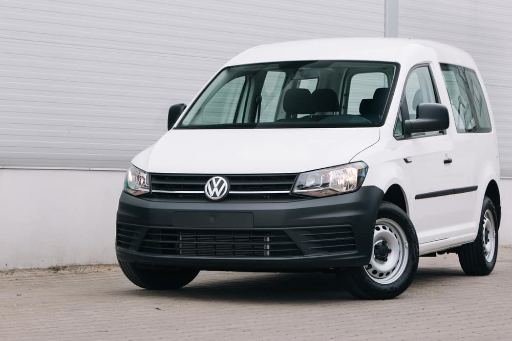 A white Volkswagen Caddy parked in front of a building, celebrating 40 years.