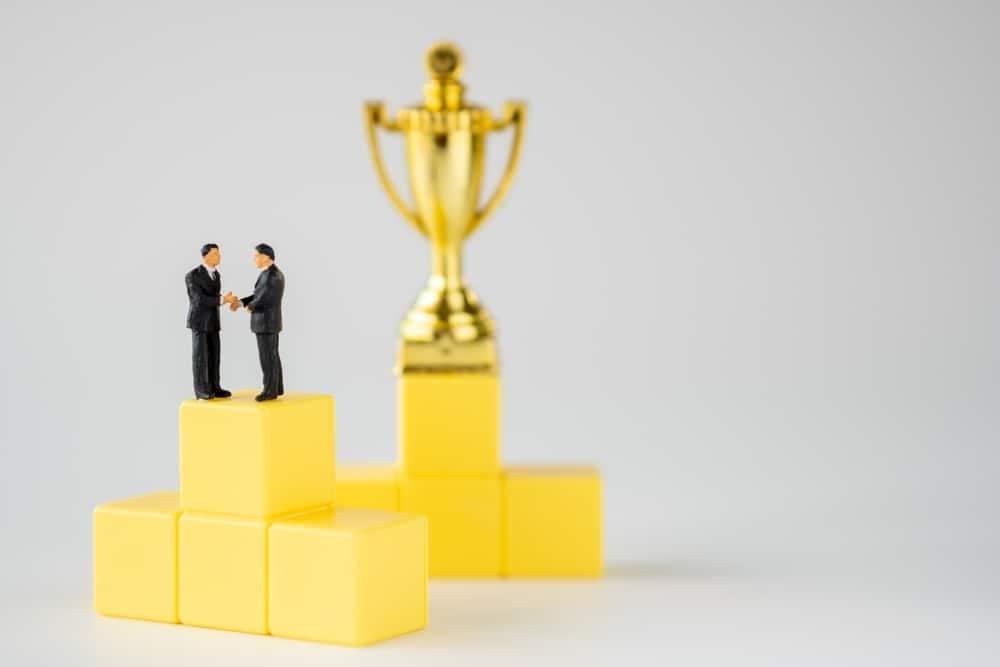 Two KEI founders, standing on top of yellow cubes, proudly display their Lifetime Achievement Award trophy.