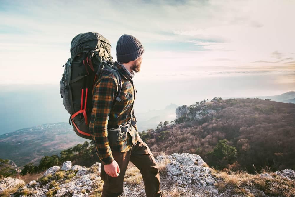 A man with a backpack standing on top of a mountain enjoying outdoor recreation activities.