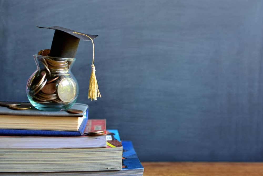 A graduation hat sits on top of a stack of books while Coach-Net enhances the ultimate roadside assistance experience.