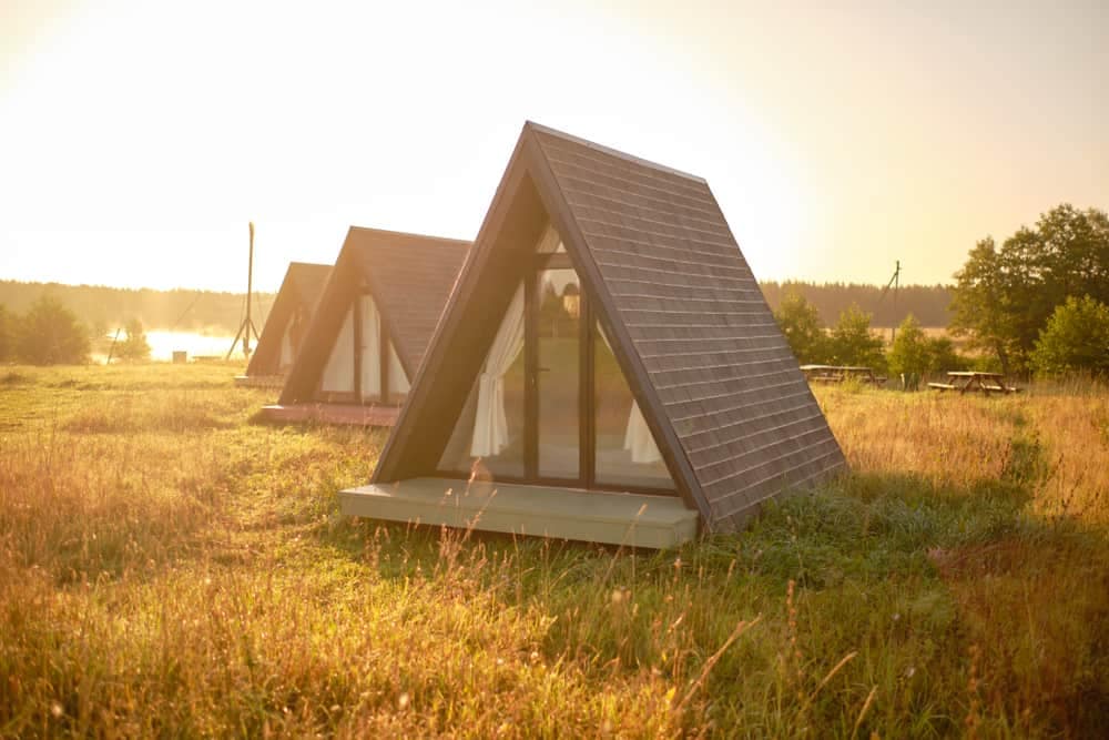 A group of glamping tents in a field near a lake.