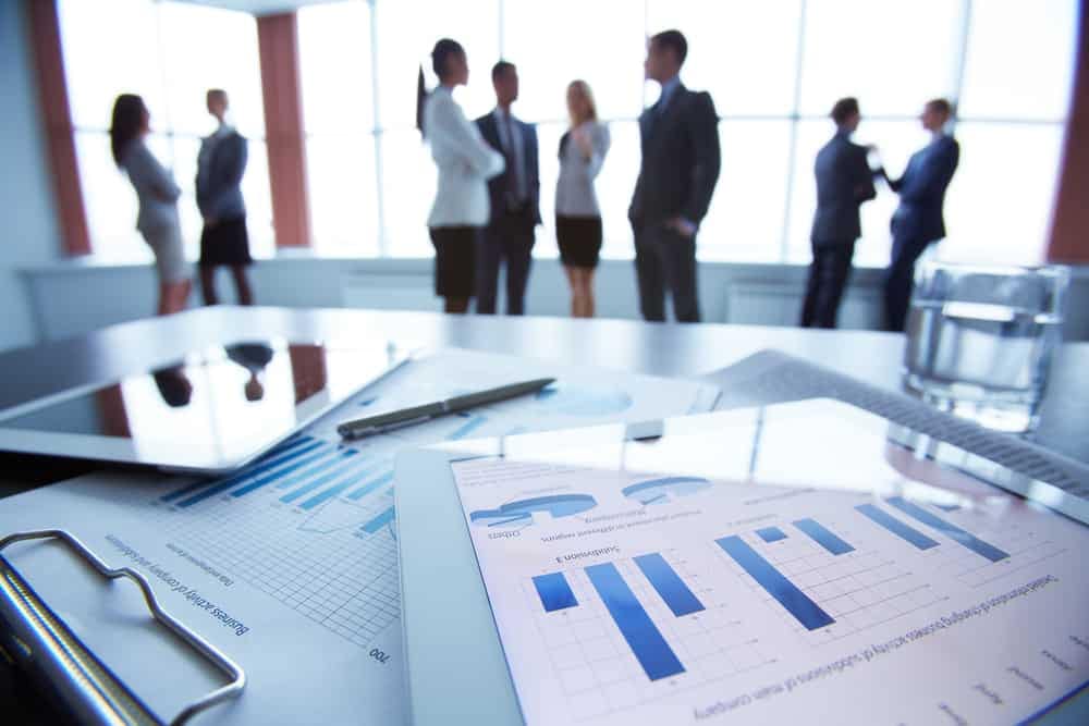 A group of business people standing in front of a tablet computer discussing the Sustainability Report.