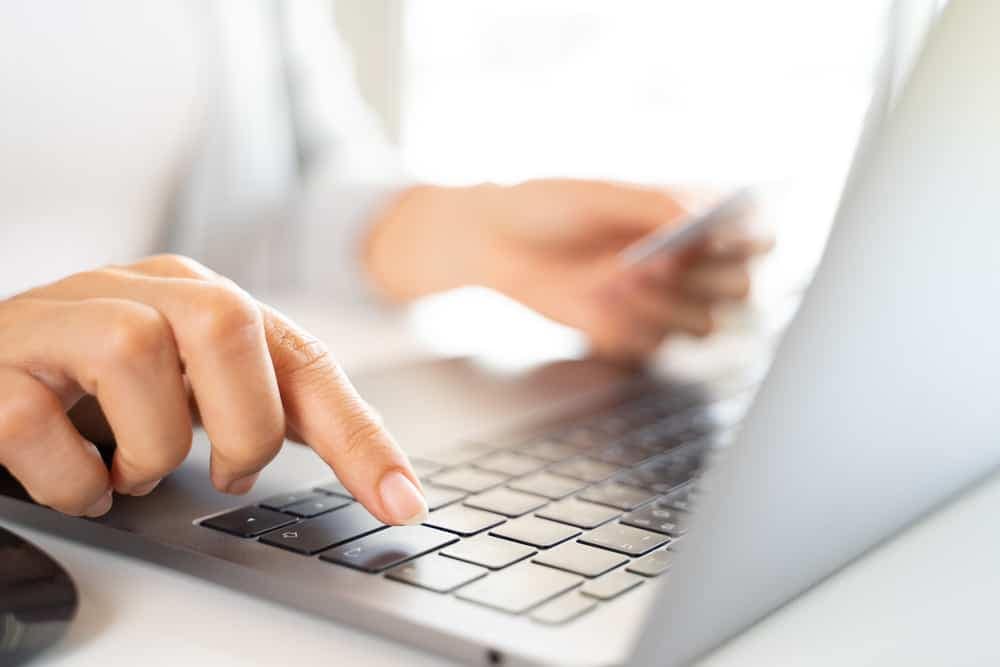 A woman's hand is typing on a laptop keyboard to complete the RoverPass and Vrbo Integration.